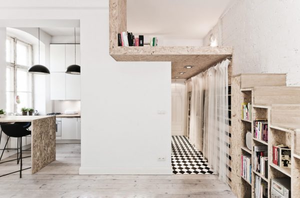 Mezzanine floor in tiny house. Image shows a 29sqm apartment with minimalistic styling. The mezzanine floor is built above the entry way and accessed via steps that double as storage space. Mezzanine creates private bedroom away from the living areas of the apartment.