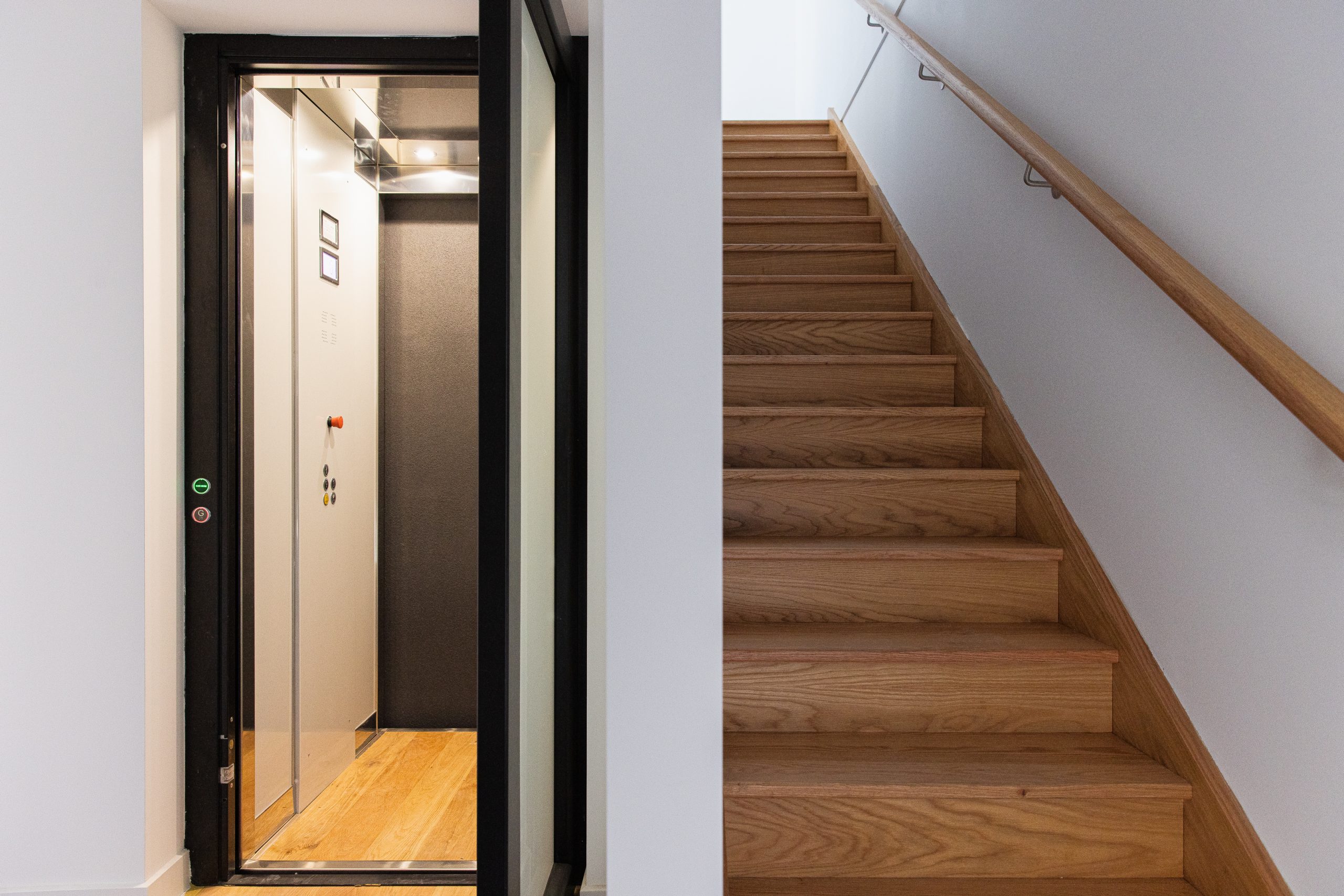 black rimmed lift with white walls and wooden flooring, next to a staircase.