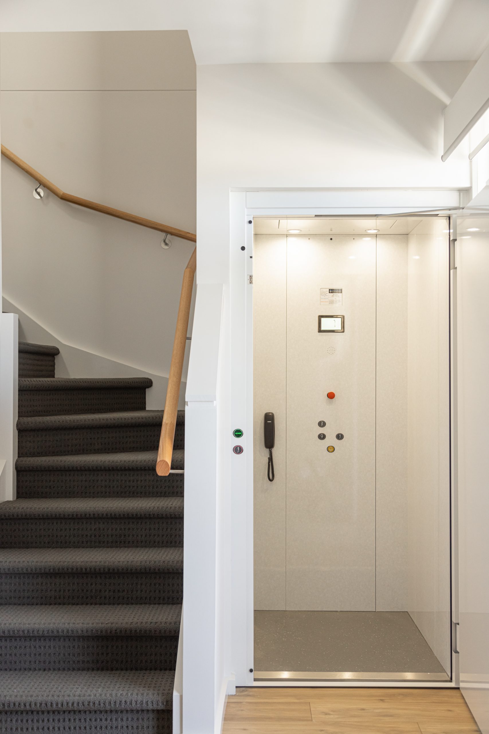 white cabin residential elevator with wooden floors next to a staircase.