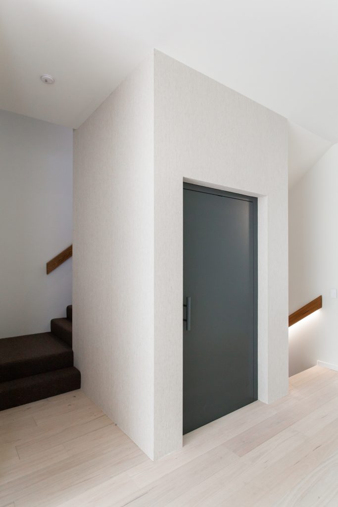 A white lift shaft with a blue door sits in between two staircases in a home.