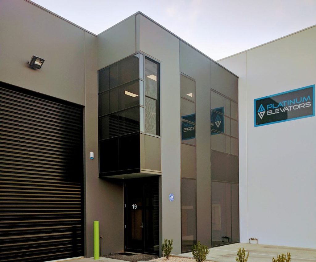 a grey commercial building with black windows and garage door. Platinum Elevators sign on wall to the right.