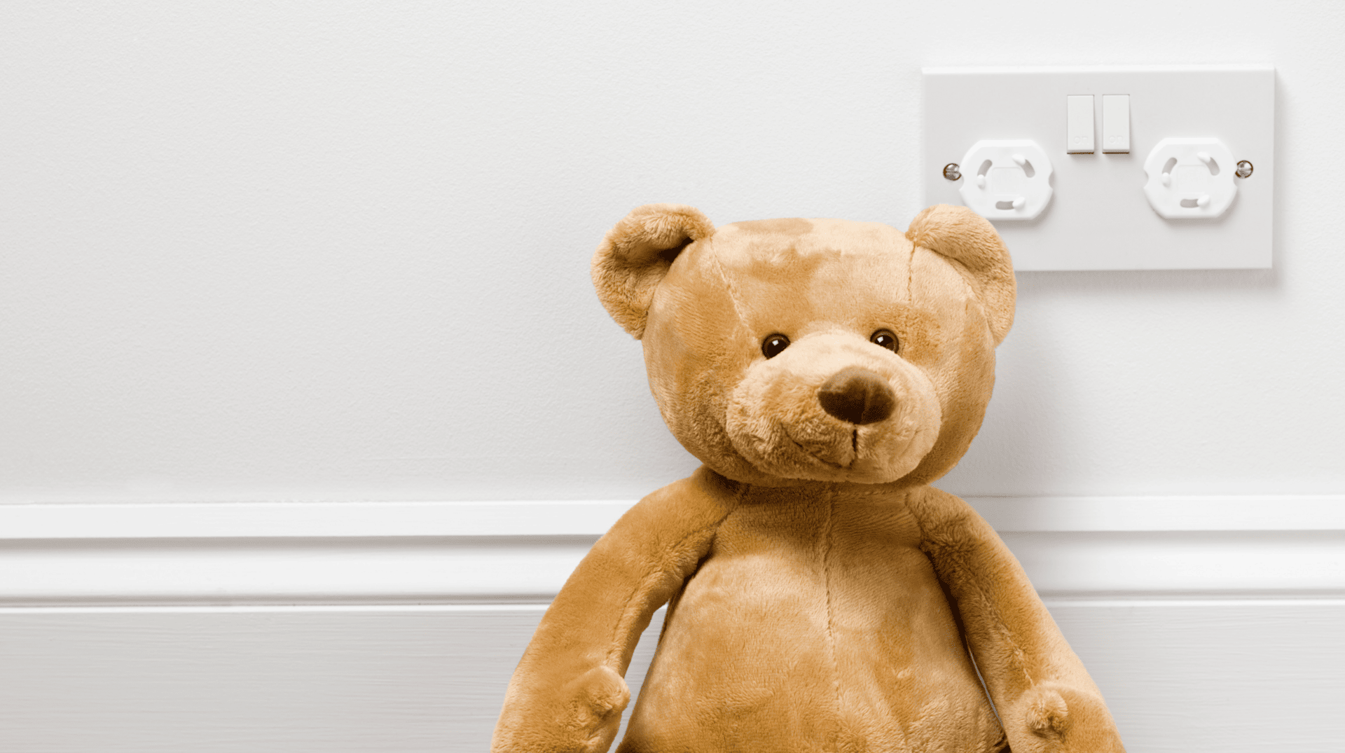 teddy bear placed in front of plug point on wall