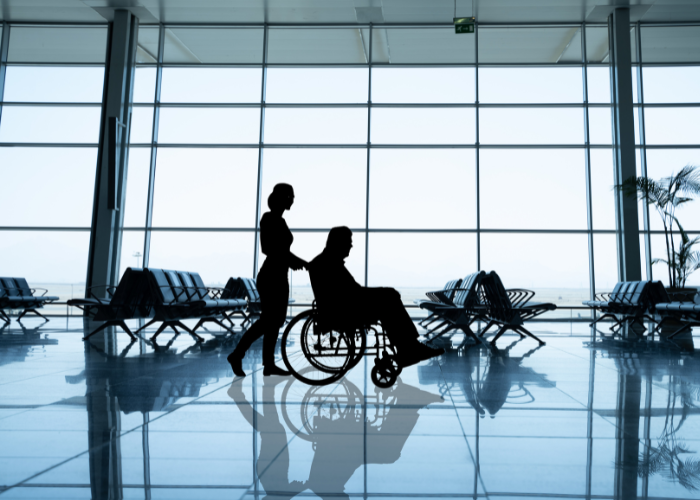 Silhouette of person pushing wheelchair in airport terminal.
