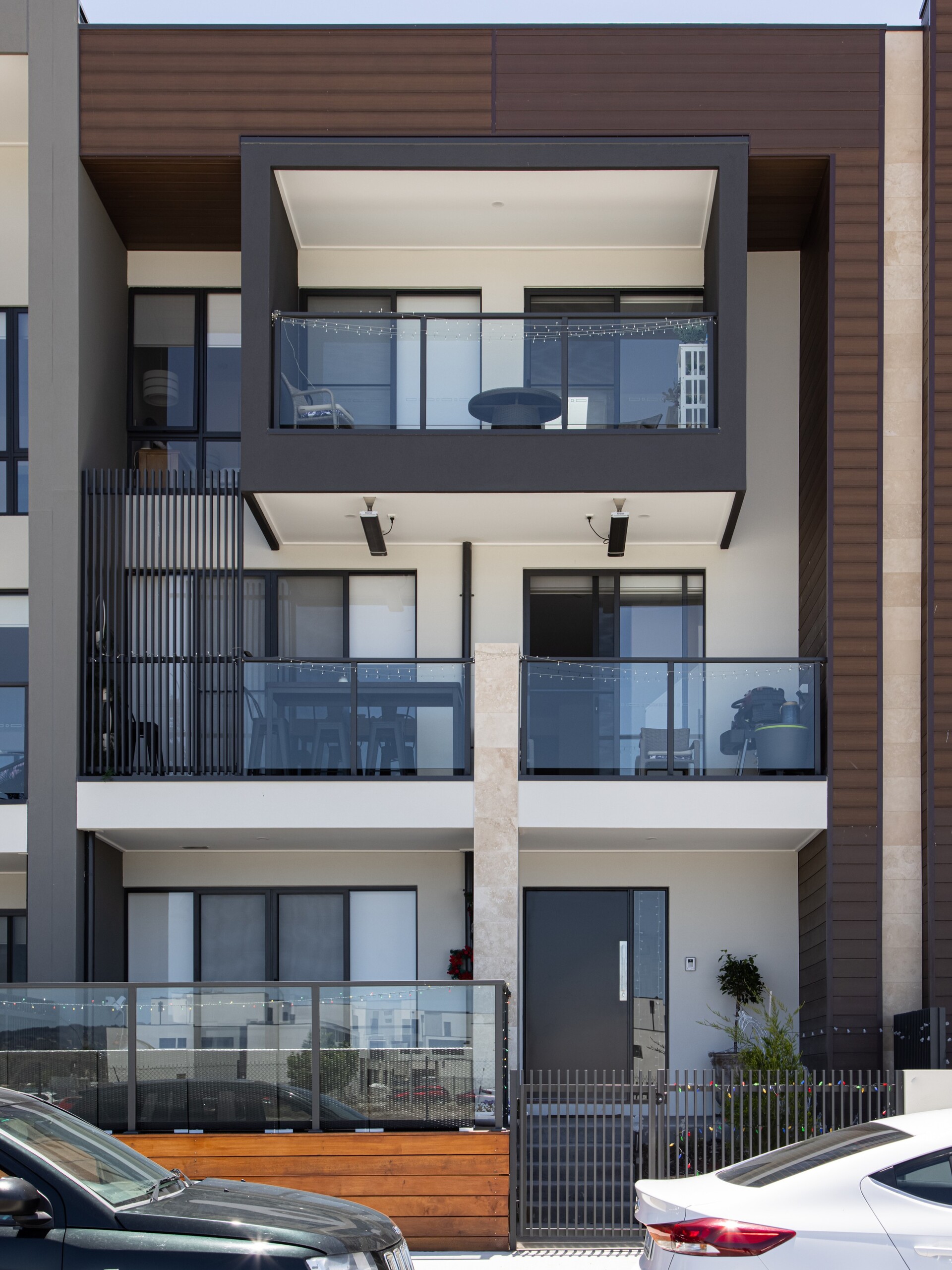Modern three-storey townhouse with balconies and parked cars.