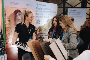 Women discussing building materials at expo booth.